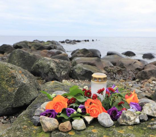 Steinküste mit Blumen und Trauerkerze